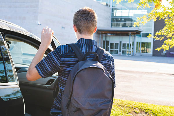 Parken auf dem Schulparkplatz: Teenager steigt vor der Schule aus dem Auto aus. 