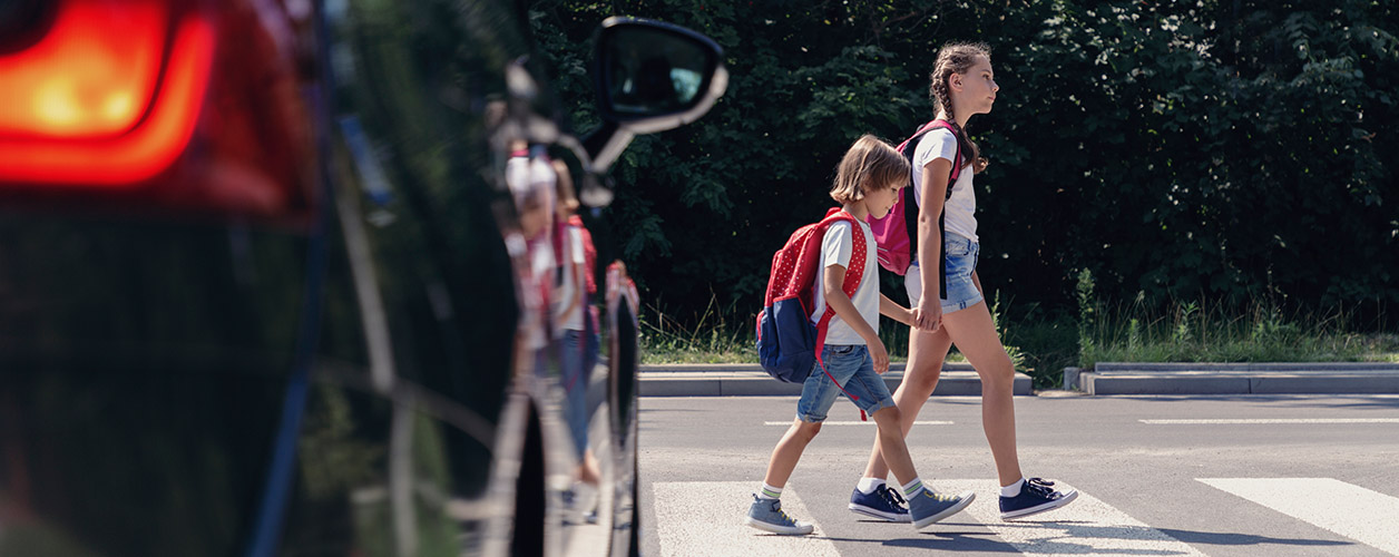 Verhalten im Straßenverkehr: Auto hält an einem Zebrastreifen, über den Schulkinder laufen.