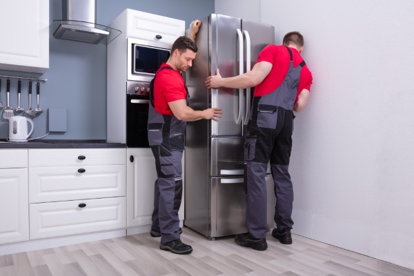 Umzugshelfer bewegen Kühlschrank vorsichtig in seiner Standposition.