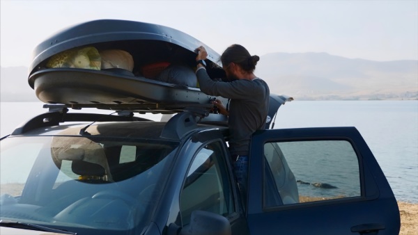 Zusätzlicher Stauraum: Mann bepackt Dachbox auf dem Autodach.