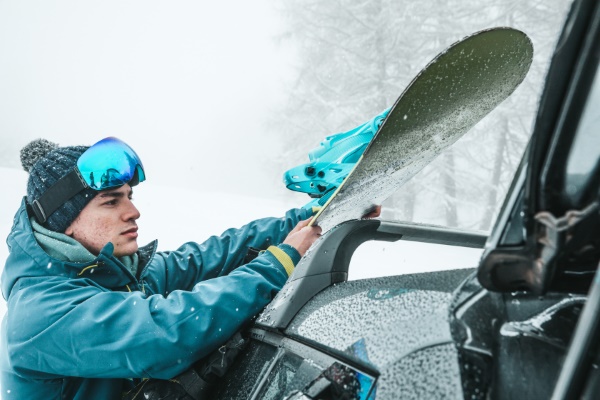 Ski auf dem Dach transportieren: Wintersportler hebt sein Snowboard aufs Autodach.