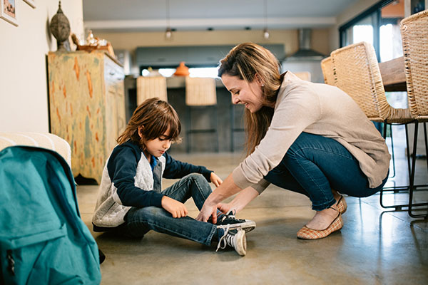 Morgenroutine Schulkind: Mutter hilft ihrem Sohn dabei die Schuhe zu binden.