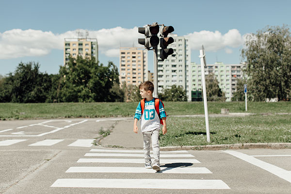 Sicherer Schulweg zu Fuß: Grundschulkind überquert den Zebrastreifen und sieht sich prüfend um.