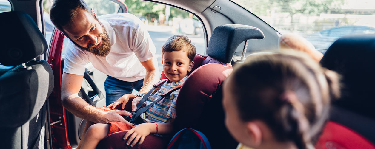 Kindersicherheit im Auto: Vater schnallt seinen Sohn im altersgerechten Kindersitz an.