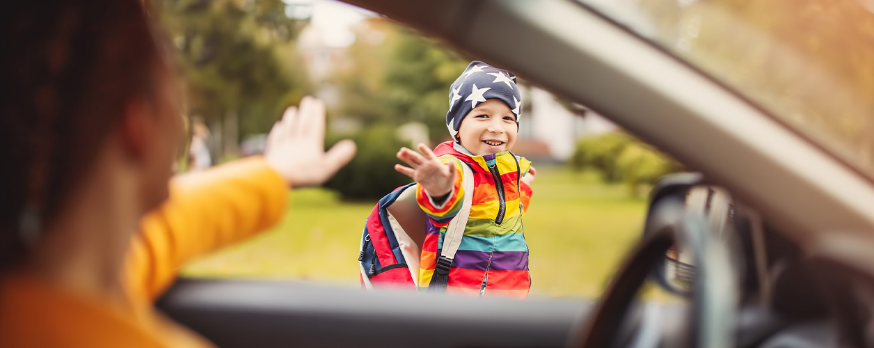 Mit Elterntaxi zur Schule: Mutter winkt ihrem Kind zum Abschied aus dem Auto zu. 