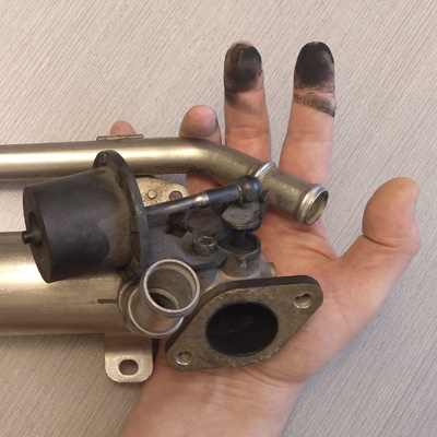 Una válvula EGR y una mano cubierta de carbonilla